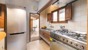 A kitchen with a stainless steel refrigerator, a gas stove, wooden cabinets, and a tiled backsplash. - Plaza maca, townhouse in the heart of Campanet (Campanet)
