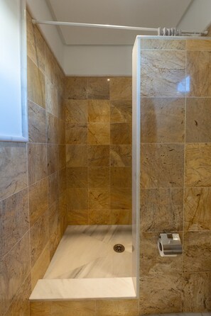 Une douche avec une porte en verre, des carreaux de marbre et un sèche-mains.