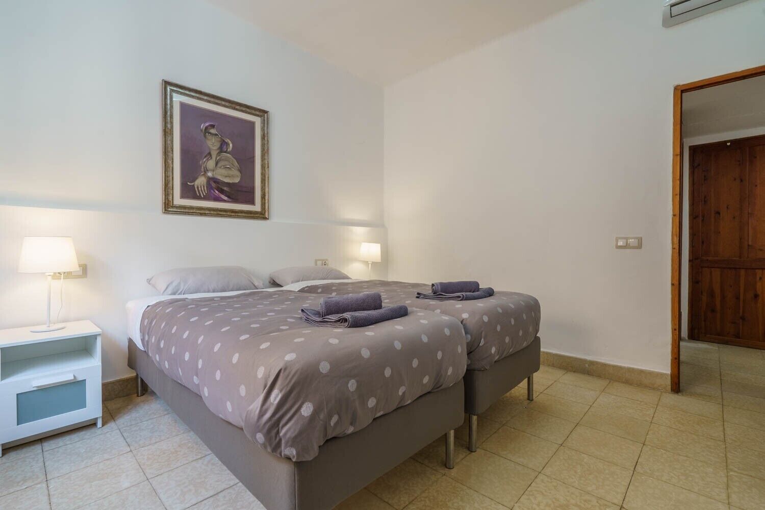 Ein Schlafzimmer mit einem Bett, zwei Nachttischen, einem Beistelltisch, einem gerahmten Bild an der Wand und einer Holztür.