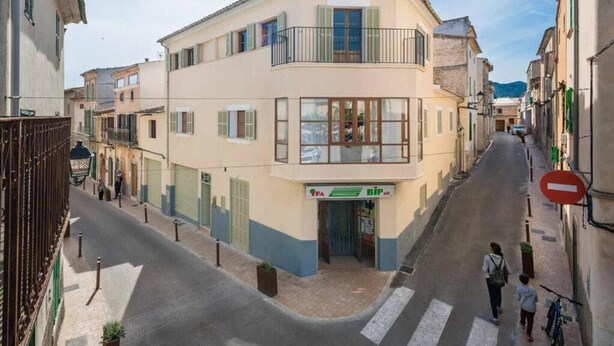 A narrow street with buildings on either side, a pedestrian crossing, and a sign for a local business.
