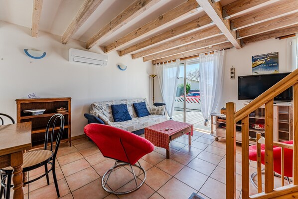 A living room with a wooden ceiling, a sofa with blue cushions, a red chair, a dining table with chairs, a TV, and a staircase. - Villa 'La Plage, Les Lacs Et Le Calme' with Private Terrace, Wi-Fi and Air Conditioning (Biscarrosse)
