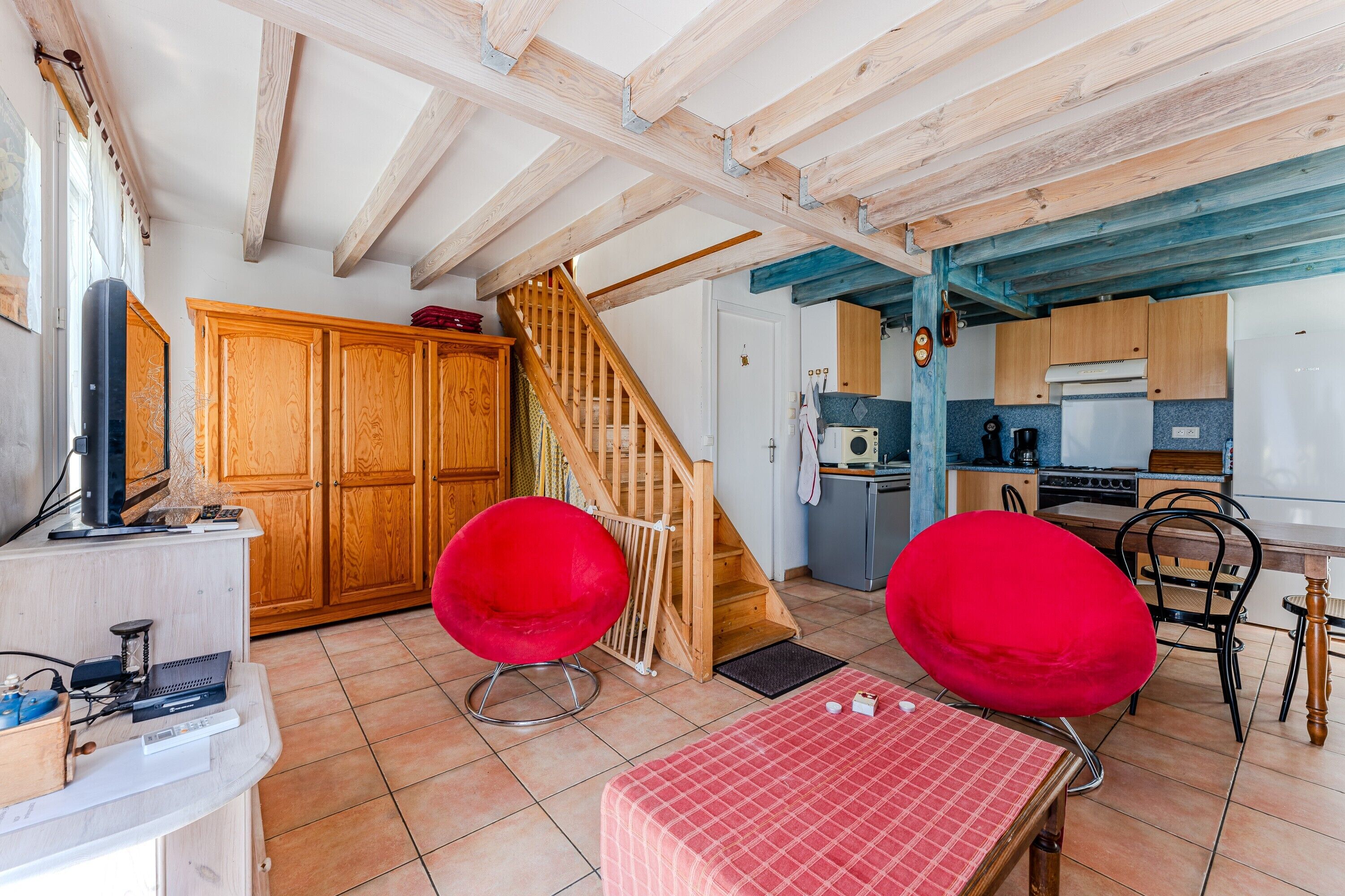Een kamer met een houten trap, een keukenhoek en twee rode stoelen.