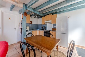 A kitchen with wooden cabinets, a white refrigerator, a wooden dining table, and a red chair. - Villa 'La Plage, Les Lacs Et Le Calme' with Private Terrace, Wi-Fi and Air Conditioning (Biscarrosse)