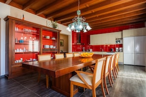 A spacious kitchen with red tiles, a wooden dining table, and a chandelier.