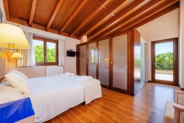 A bedroom with a wooden ceiling, a bed with white linens, a bedside lamp, a TV, and a sliding glass door leading to a balcony. - Country House 'Conies Salvia' with Private Pool, Wi-Fi and Air Conditioning (MANACOR)