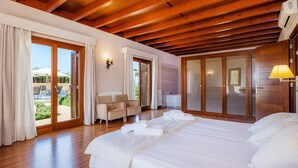 A hotel room with wooden beams, a bed with white linens, a sofa, a bathroom, and a sliding glass door to the outside. - Country House 'Conies Salvia' with Private Pool, Wi-Fi and Air Conditioning (MANACOR)