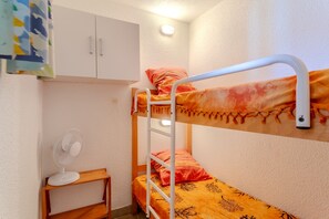 Ein Stockbett mit einer Stehle, ein weißer Ventilator auf einem kleinen Tisch und ein weißes Schränkchen.