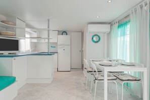 A compact kitchen with white cabinetry, a refrigerator, a dining table with chairs, and a window with curtains.