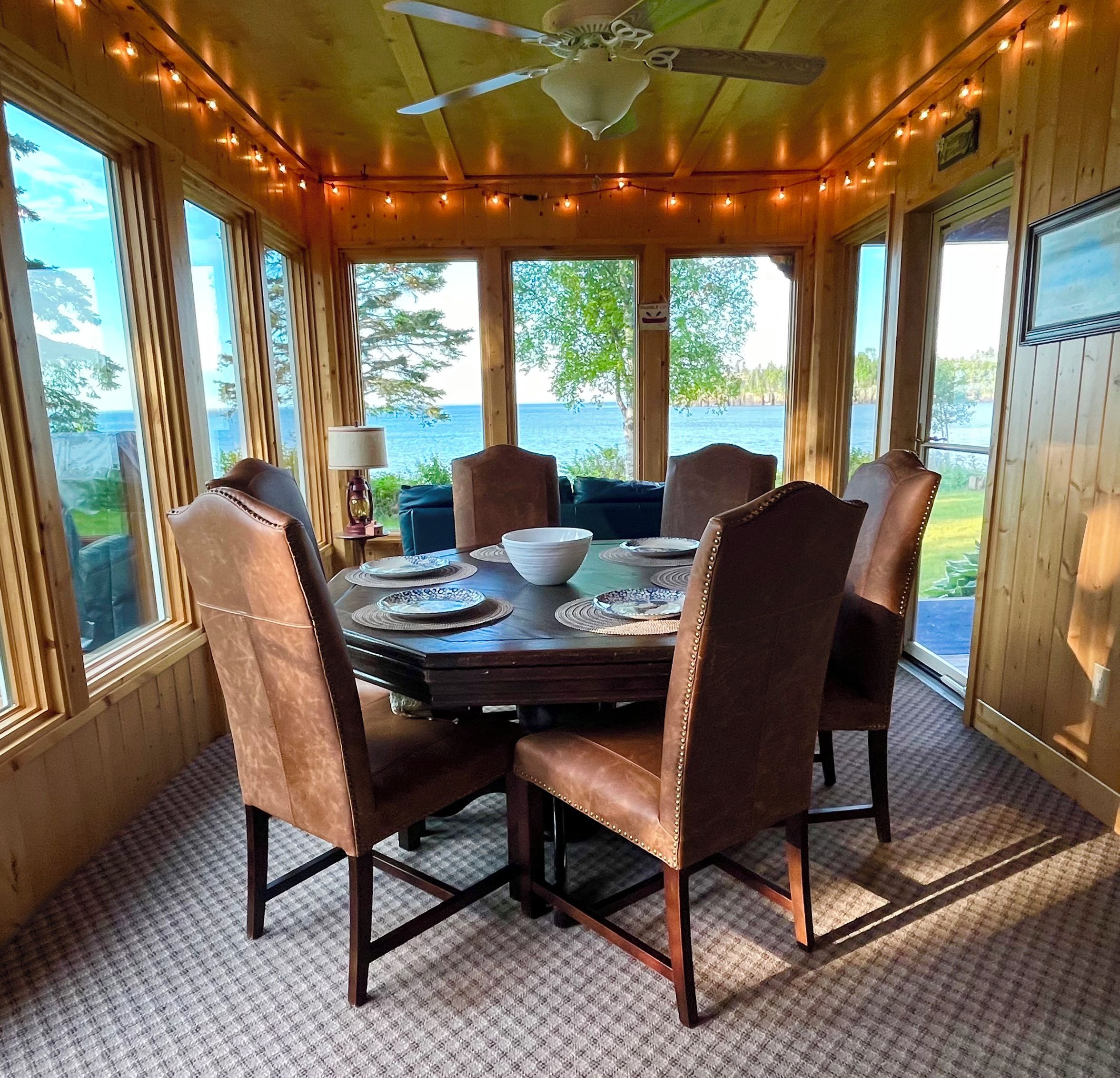 Une salle à manger aux murs lambrés, avec une table dressée pour quatre personnes, de grandes fenêtres et un ventilateur de plafond.