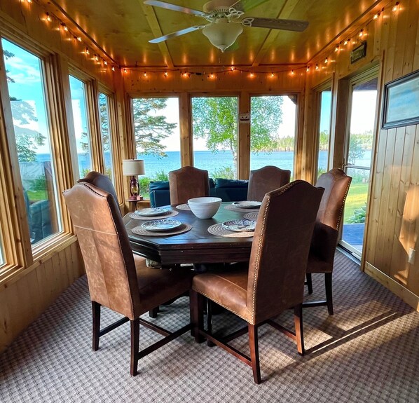 Un comedor con paneles de madera, una mesa dispuesta para cuatro, ventanas amplias y un ventilador de techo.
