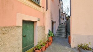 A narrow alley with a green door, potted plants, and a staircase leading to a building.