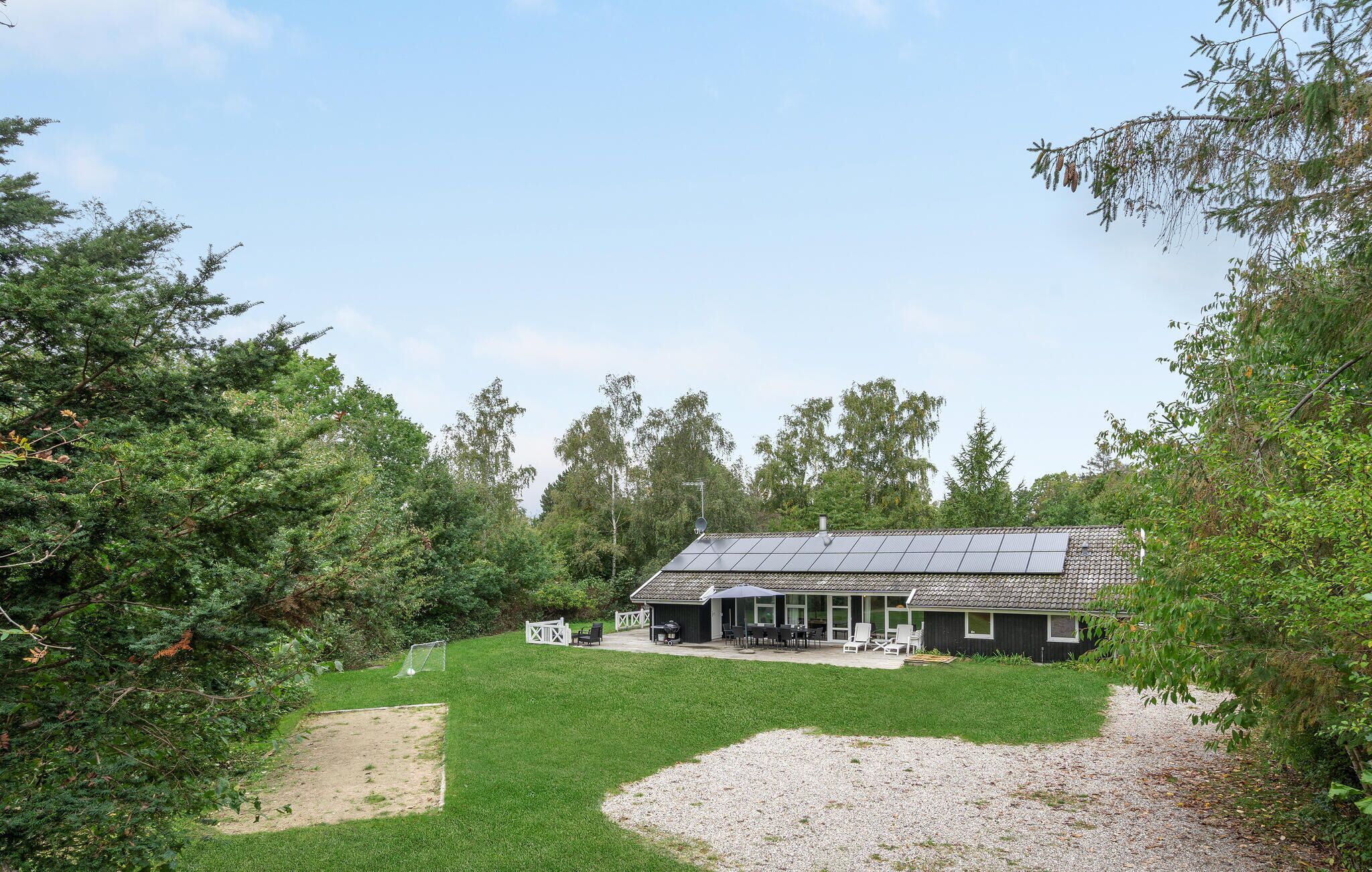 Een woning met een dakbedekt met zonnepanelen, een terras met tuinmeubilair en een verzorgd gazon.