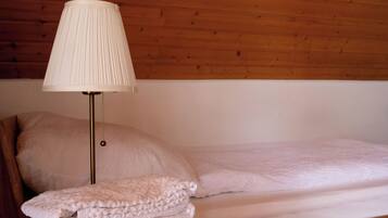 A neatly made bed with a white comforter and pillows, a lamp with a white shade, and a stack of folded towels.