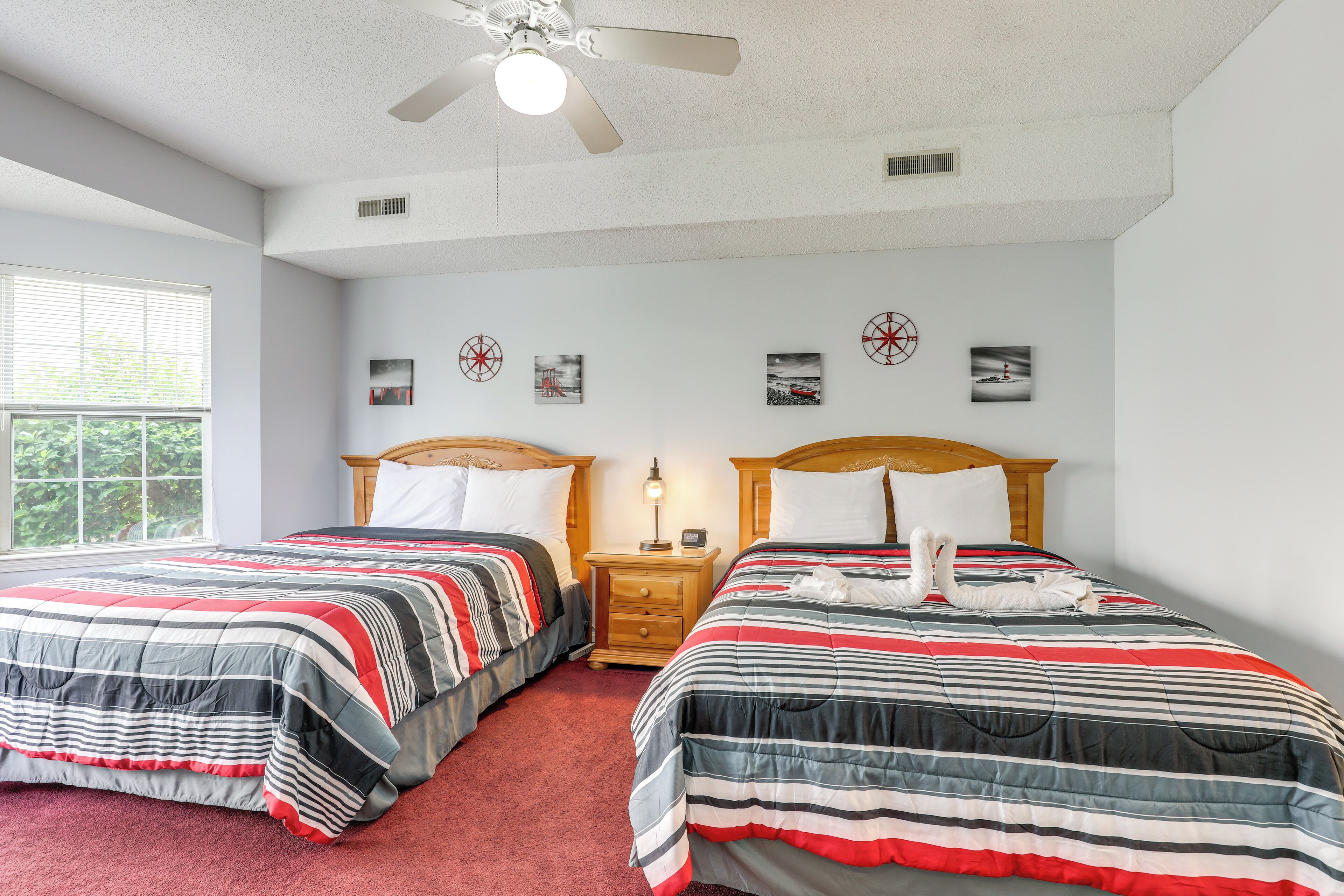 A hotel room with two beds, a ceiling fan, and artwork on the walls.