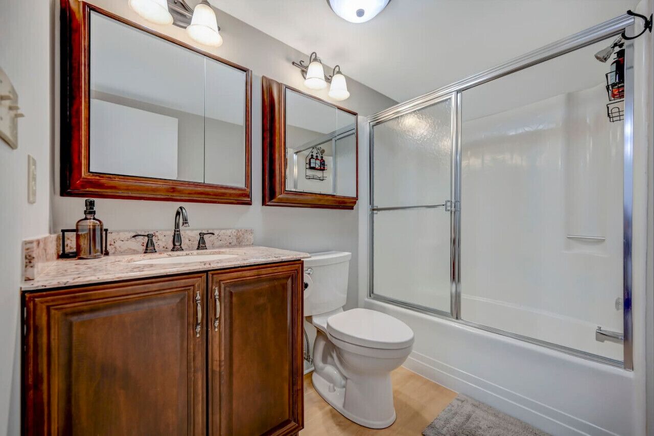 A bathroom with a vanity, two mirrors, a toilet, and a glass-enclosed shower.