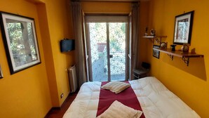 A hotel room with a bed, a television, a radiator, a window with a view, and a shelf with decorative items. - LunaBedRoma - Short rentals in the green (Roma)