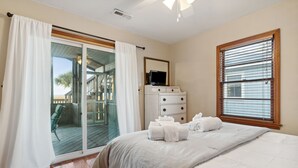 Une chambre avec un grand lit, une commode, un téléviseur posé sur un meuble et une porte-fenêtre coulissante donnant sur une terrasse extérieure.
