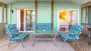 Un espace extérieur abrité, aménagé avec deux chaises et une table, un ventilateur de plafond et une vue sur la pièce adjacente.