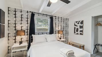 Ein ordentlich bezogenes Bett mit weißen Laken, zwei Nachttischlampen, ein Deckenventilator und ein Fenster mit Jalousien.
