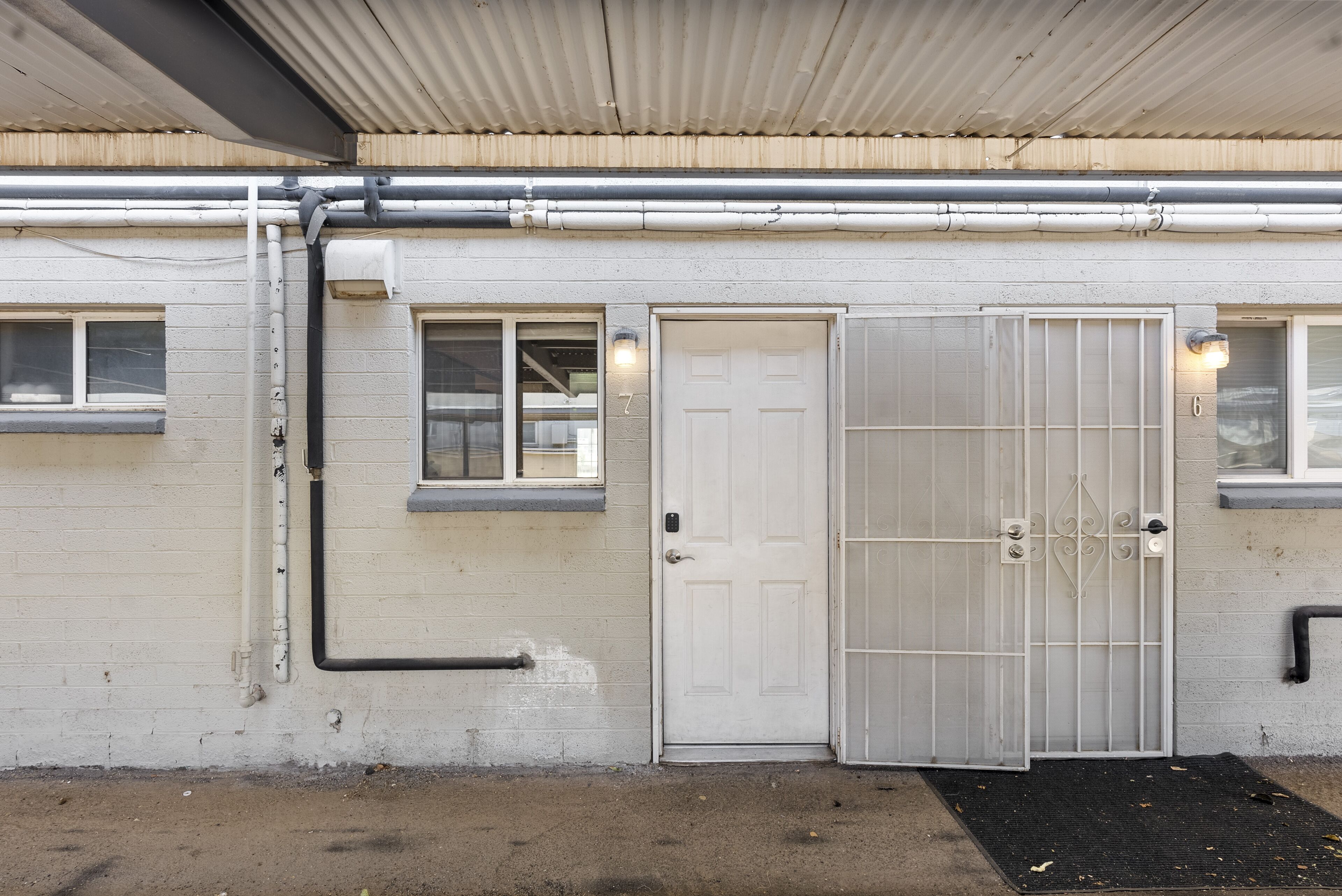 A building with a white exterior, a white door with a metal gate, and a black mat at the entrance.