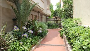 A narrow pathway flanked by lush greenery and a building with a tiled walkway. - Ostia-apartment 50 mt from the beach, near historic center-sea view (Lido di Ostia)