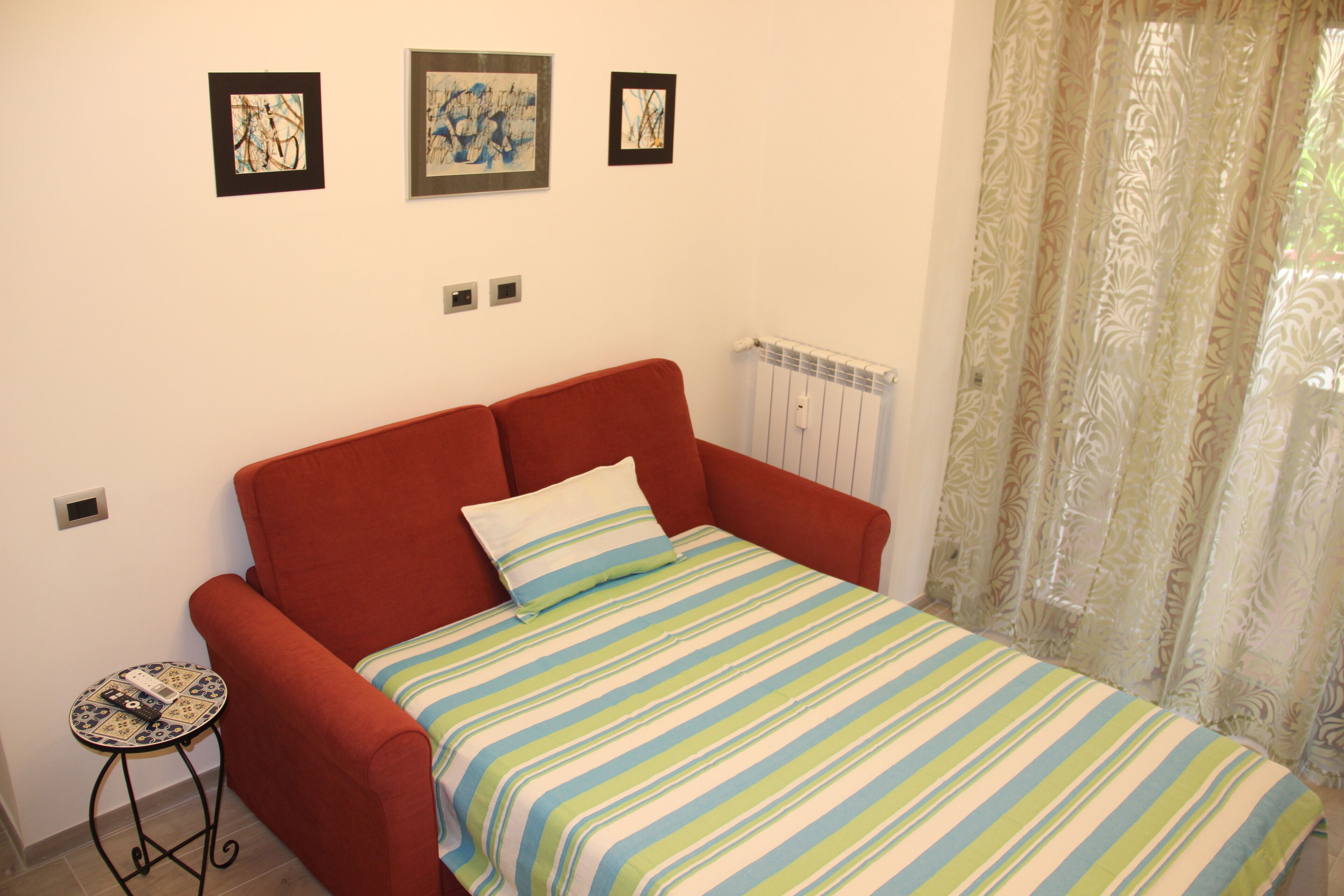 Una habitación con un sofá rojo, un edredón a rayas y tres cuadros enmarcados en la pared.
