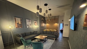Una sala moderna con un sofá seccional, dos sillones, una mesa de centro y una zona de comedor con una mesa preparada para cuatro personas.