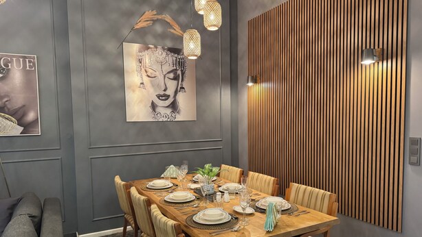 Comedor con mesa de madera dispuesta para seis personas, paredes grises y panel de madera vertical.