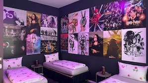 Un dormitorio con dos camas, una pared llena de carteles y una iluminación morada.