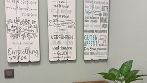 Tres letreros colocados en la pared con mensajes motivacionales en alemán, una mesa de madera y una planta en maceta.