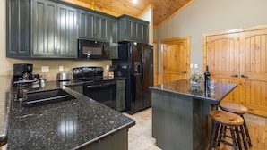 A kitchen with dark cabinets, a black refrigerator, a coffee maker, and a wooden door. - Private Hot Tub Getaway with Peaceful Views, Free Silver Dollar Tickets & Near Branson Shows (Branson)