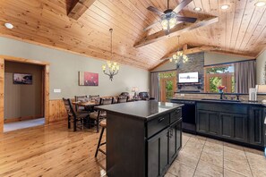 A spacious kitchen with a large island, wooden ceiling, and a dining area with chairs and a table.