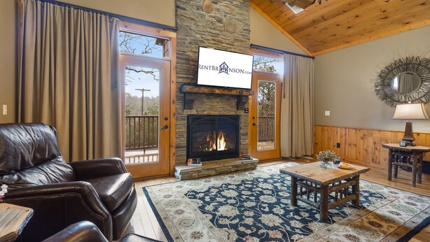 A cozy living room with a stone fireplace, leather sofa, and a large rug. - Private Hot Tub Getaway with Peaceful Views, Free Silver Dollar Tickets & Near Branson Shows (Branson)
