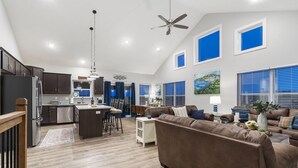 A spacious living area with a brown leather sofa, a dining table with chairs, a kitchen with dark cabinets, and a ceiling fan. - Lake View Condo with Private Hot Tub, $400 Free Daily Tickets & Unique Layout (Kimberling City)