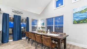 A dining area with a long wooden table, brown leather chairs, and a view of the ocean through large windows. - Lake View Condo with Private Hot Tub, $400 Free Daily Tickets & Unique Layout (Kimberling City)