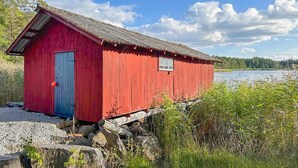 Una estructura de madera roja con una puerta azul, ubicada en una orilla rocosa junto a un lago.