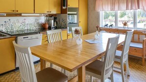Una cocina con armarios amarillos, una mesa de madera, sillas blancas y un ventanal con vistas al exterior.