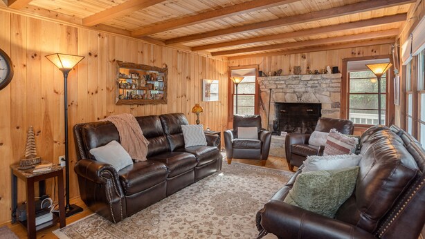 Ein gemütliches Wohnzimmer mit Holzwänden und -decke, ausgestattet mit einem Ledersofa, Sesseln, einem Kamin und einem Kaminverkleidung aus Stein.