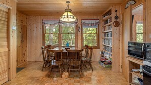 Ein Holzinterieur mit Esstisch und Stühlen, einer Kristallleuchter, Bücherregalen und einer Mikrowelle.