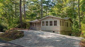 Eine Holzhütte mit Kiesweg und kleiner Veranda, umgeben von dichtem Wald.