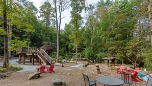 Ein rustikaler Sitzbereich im Freien mit Adirondack-Stühlen, einem Holztisch und einer kleinen Holzhütte.