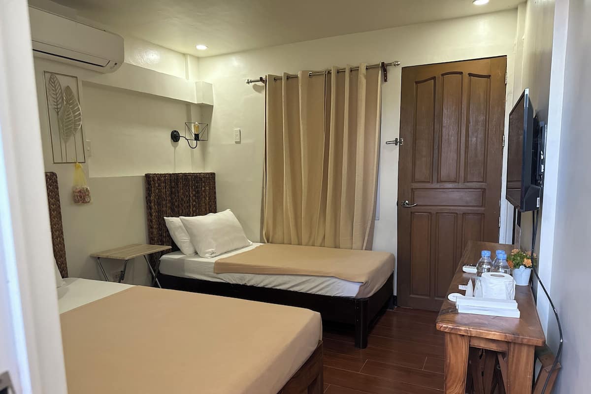 A hotel room with two beds, a wooden desk with toiletries, a TV, and a wooden door.