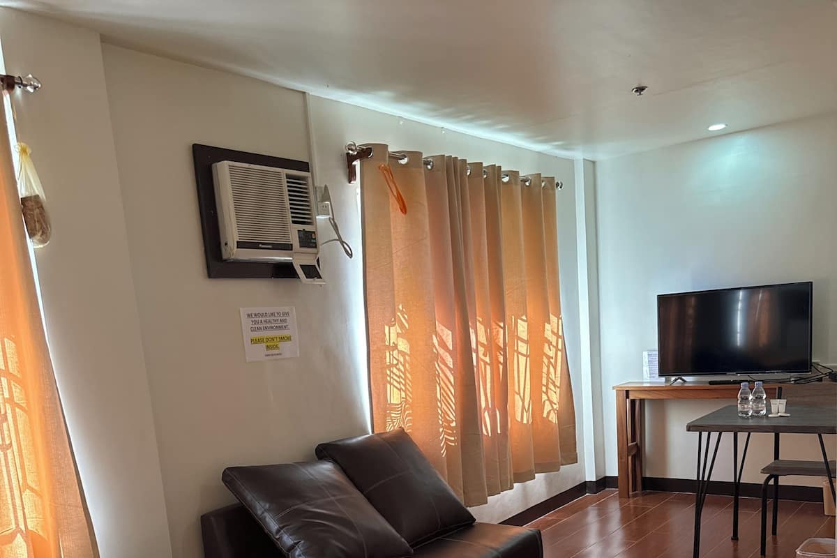 A hotel room with a sofa, a TV, a small table with water bottles, and a trash bin.