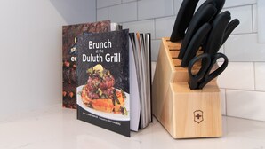 A kitchen counter with a book titled 'Brunch at the Duluth Grill' and a knife block with black-handled knives.