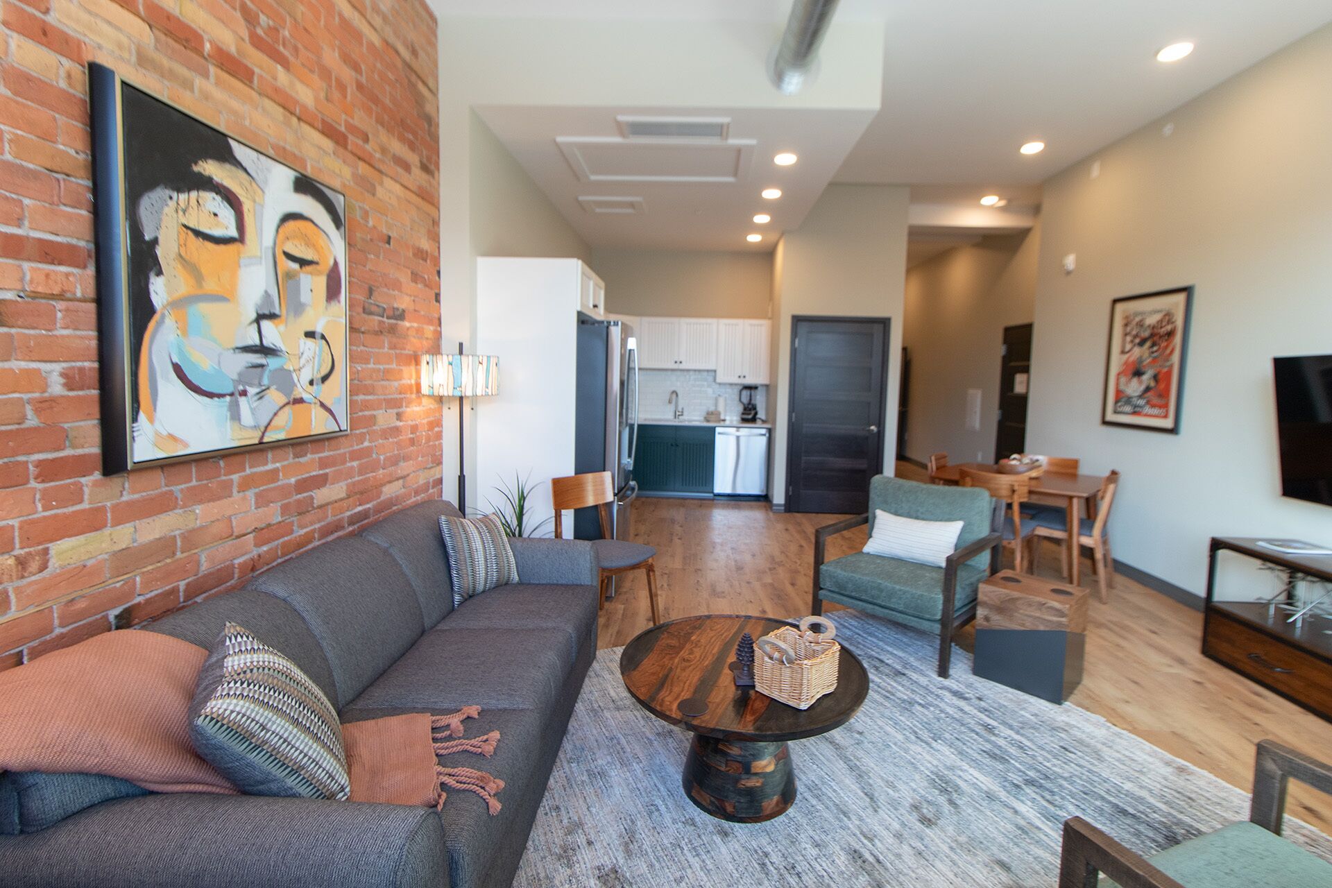 A modern living room with a sofa, coffee table, and chairs. There is a kitchen in the background with white cabinets and a dishwasher.