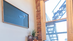 A modern office space with a desk, two chairs, a potted plant, and a window with a view of a building. - Luxury Craft District Suites | Unit 102 (Duluth)