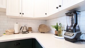 Eine moderne Küche mit weißen Schränken, einem eingebauten Mixer und verschiedenen Küchenutensilien auf der Arbeitsfläche.