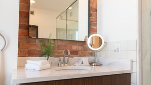 Un baño con lavamanos blanco, espejo, planta y un mueble de madera.