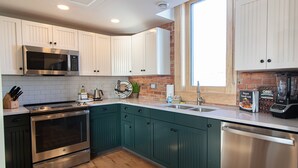 Una cocina moderna con electrodomésticos de acero inoxidable, armarios color turquesa y una pared decorada con ladrillo.