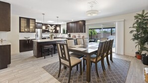 Une cuisine moderne avec des meubles de couleur sombre, un îlot central et un coin repas comprenant une grande table et des chaises.